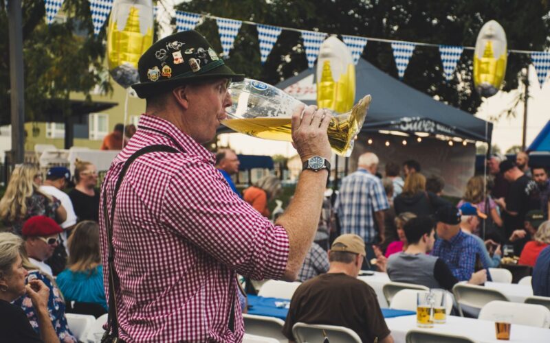 Man enjoying a large beer mug at an Oktoberfest celebration outdoors with a lively crowd.