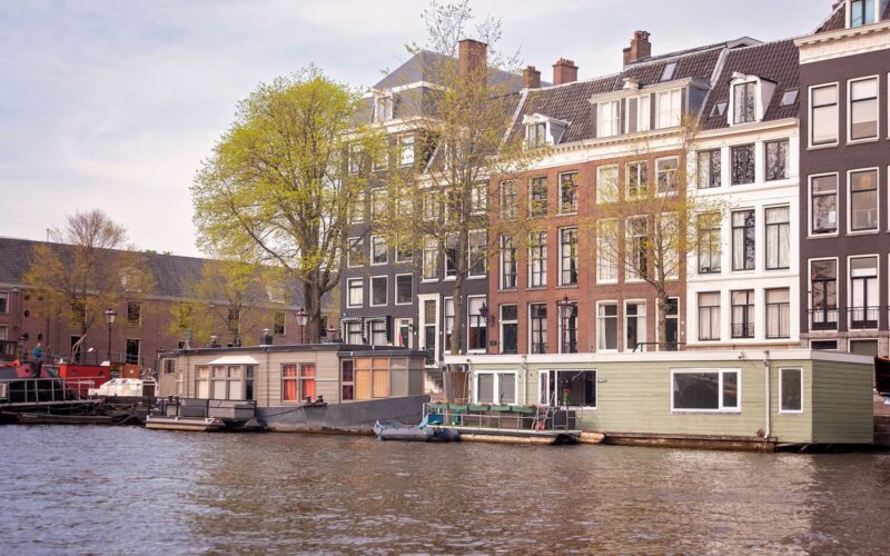 Scenic view of Amsterdam canal with historic buildings and houseboats under a clear sky.