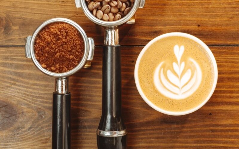 Espresso portafilters with coffee beans and latte art on wood surface.