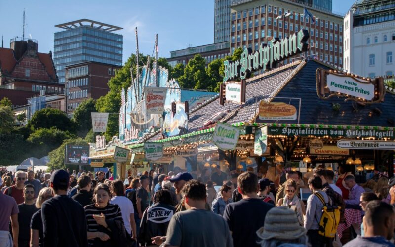 A bustling street festival in Hamburg with crowds enjoying food stalls under a blue sky.
