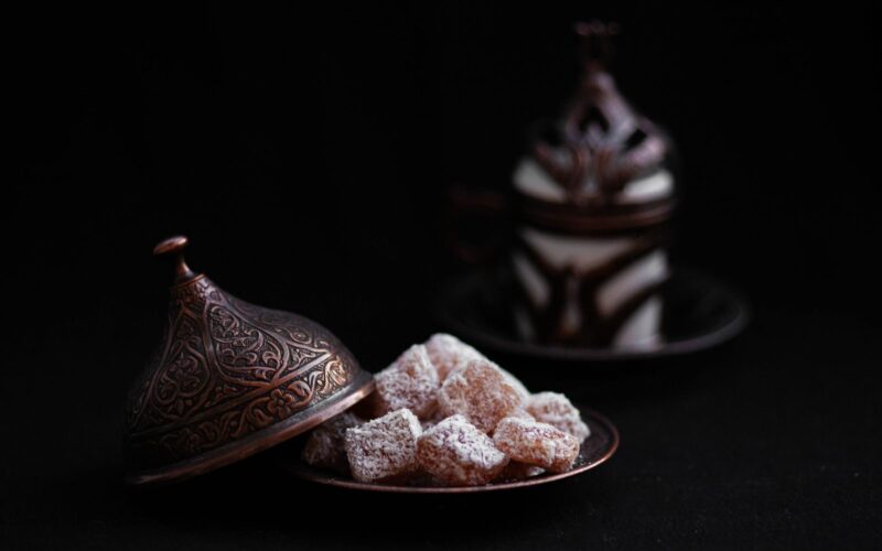 A close-up of Turkish delight in an ornate copper dish with a traditional coffee cup in the background.