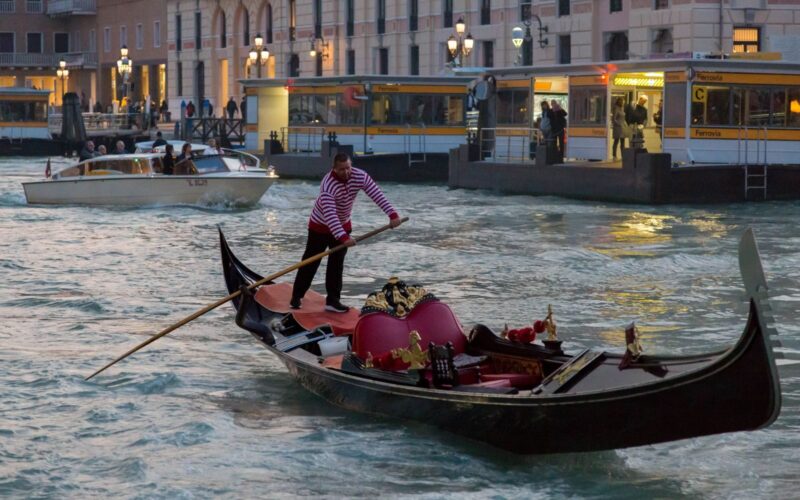A gondolier navigates a gondola on a Venetian canal in the evening light, offering a glimpse of traditional Venice.