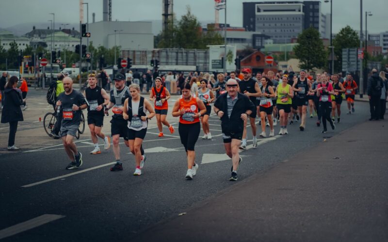 Energetic runners in Belfast marathon on urban streets with cheering spectators.