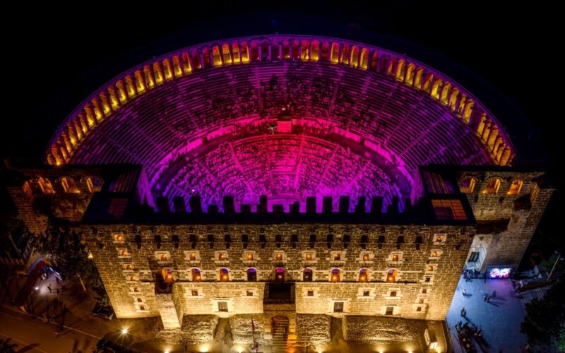 A breathtaking aerial shot of the illuminated Aspendos Amphitheater in Antalya, showcasing vibrant colors at night.