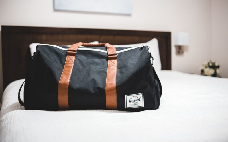 Contemporary baggage bag with inscription on white bed cover in light hotel room