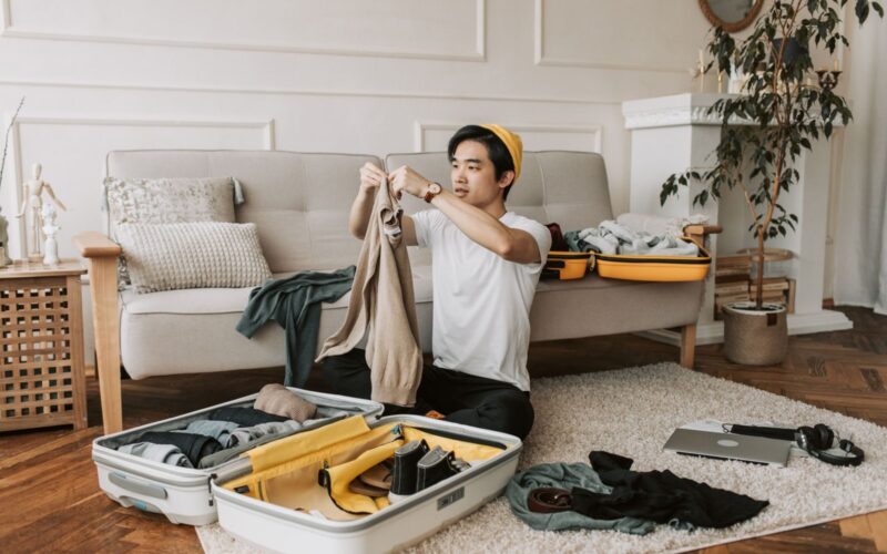 A young man organizes clothes into a suitcase in a stylish living room, preparing for a trip.