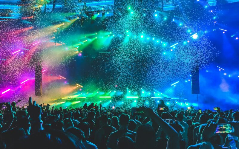 Kalabalık bir konser alanında renkli sahne ışıkları ve izleyiciler