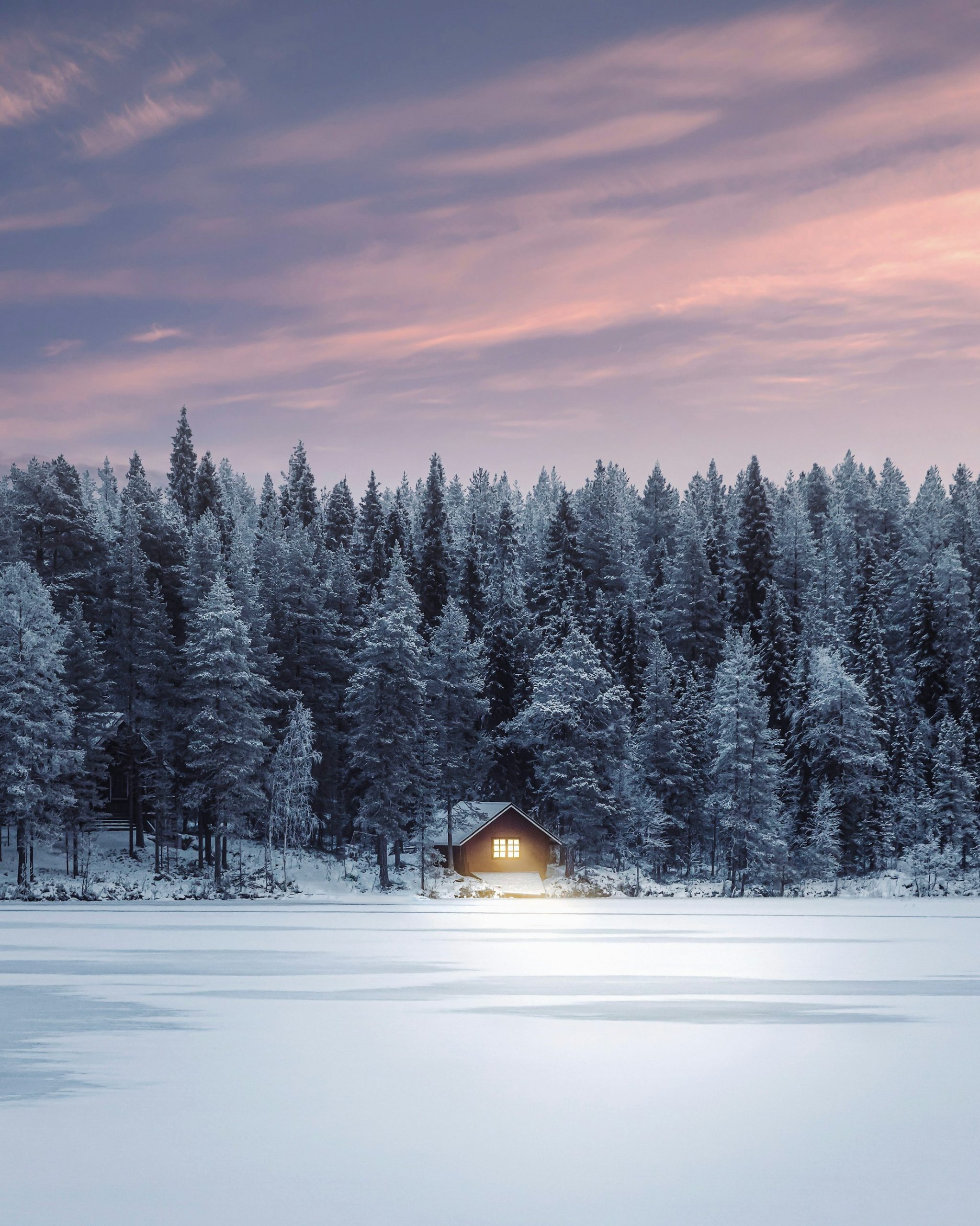 Lapland’da karla kaplı ormanın ortasında ışıkları yanan küçük bir ahşap kulübe