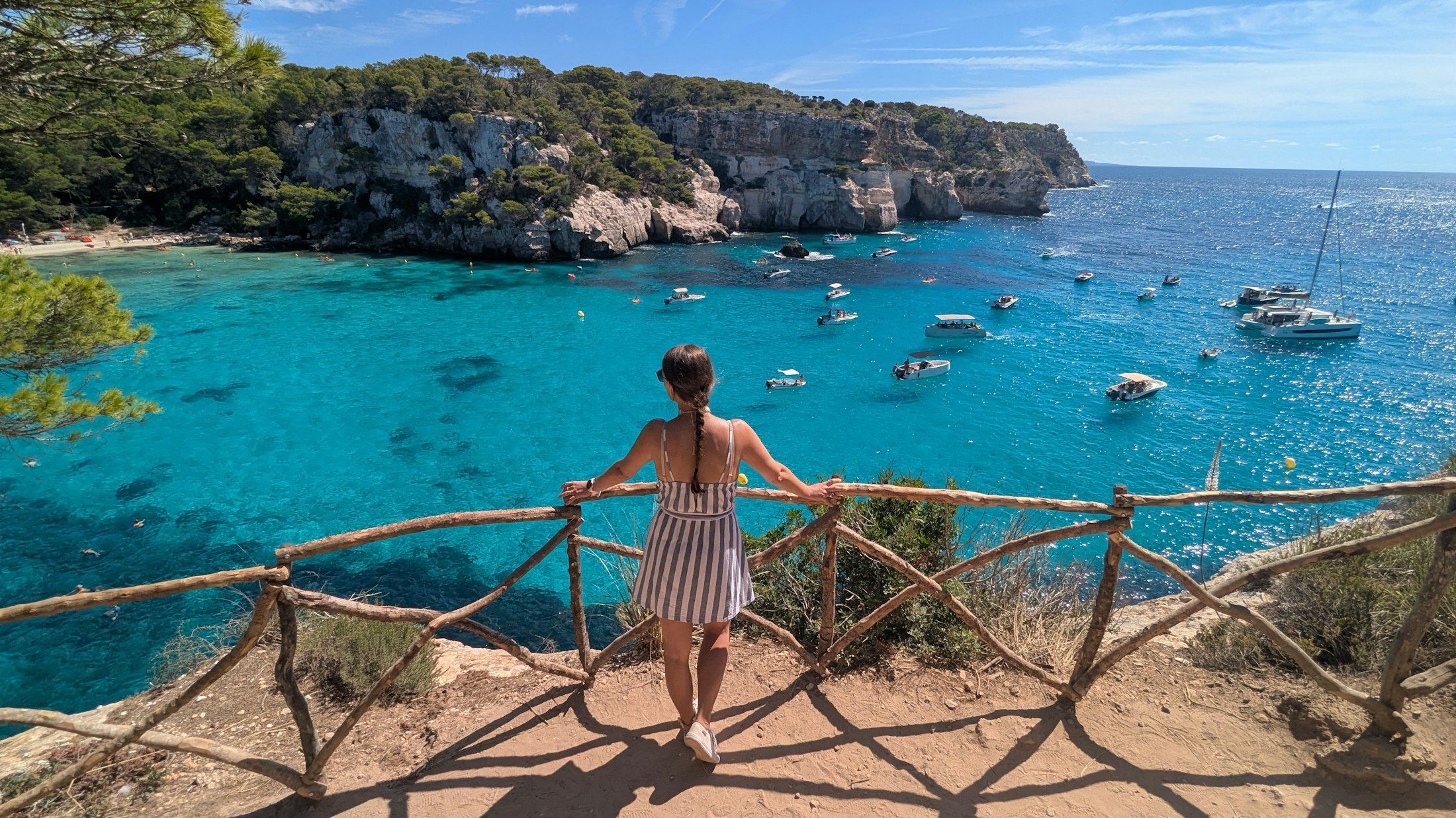 Menorca’daki Cala Macarella koyuna bakan bir ziyaretçi ve berrak turkuaz deniz