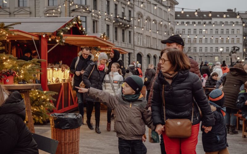 Zürih’te ışıklar altındaki Noel pazarı ve ahşap stantlarda dolaşan ziyaretçiler